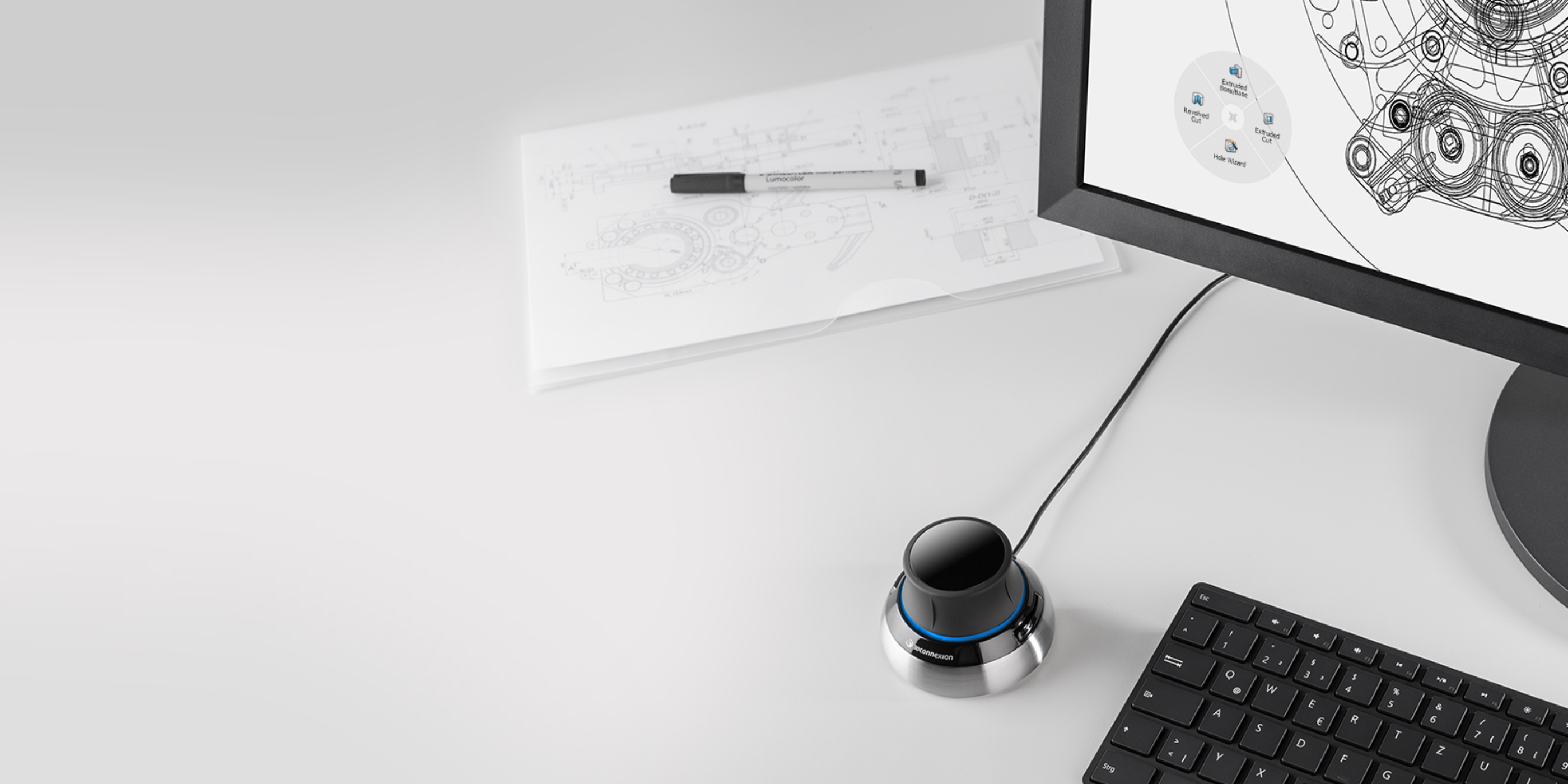 Easy to use: The SpaceMouse Compact is shown on a desk beside a keyboard and a monitor displaying a 3D model. The device features two buttons, each opening its own 3Dconnexion radial menu, providing access to up to 8 favorite commands. The 3DxWare 10 software allows users to create custom radial menus or choose from presets.