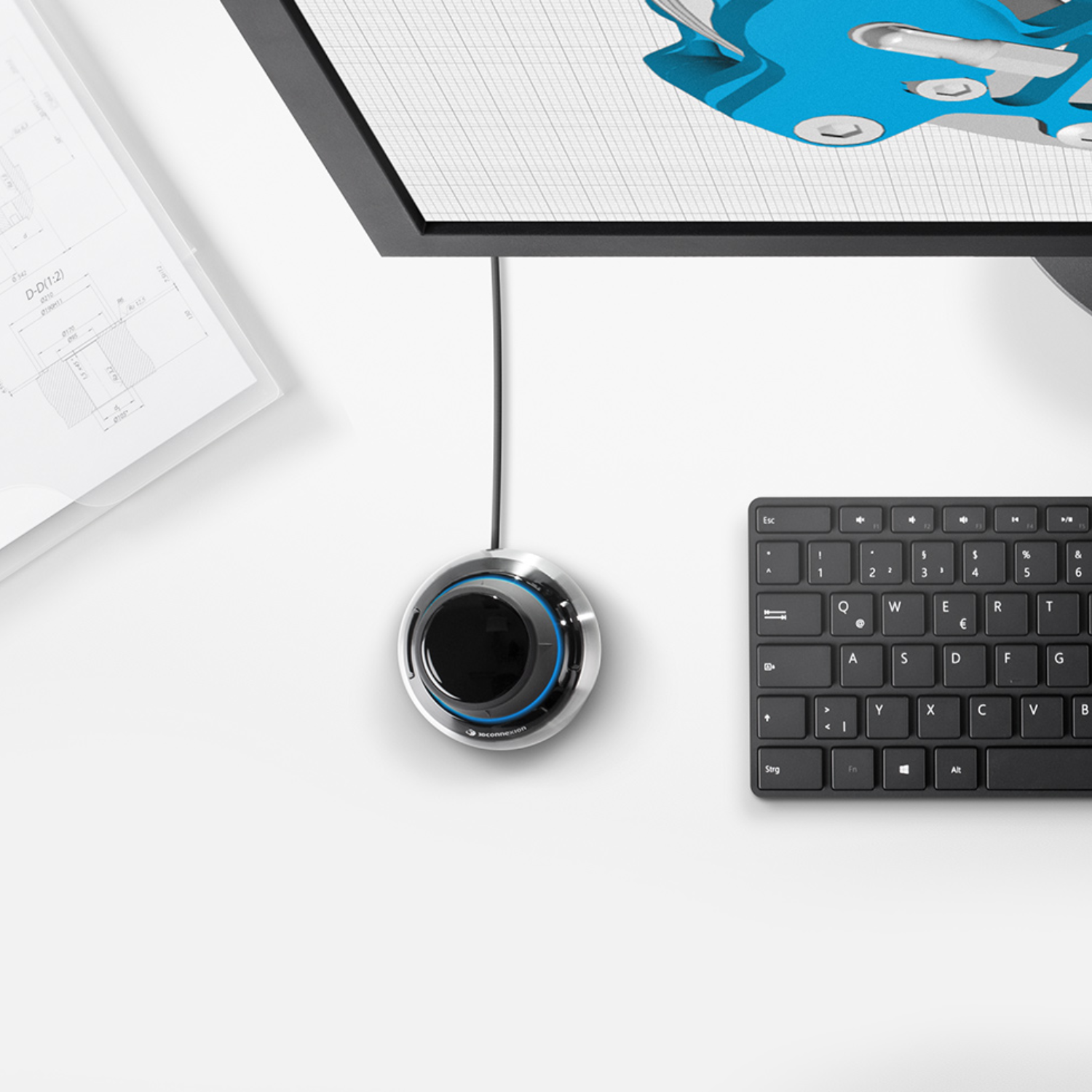 Top view of the 3Dconnexion SpaceMouse® Compact on a desk next to a keyboard and monitor displaying a 3D model, emphasizing precision.
